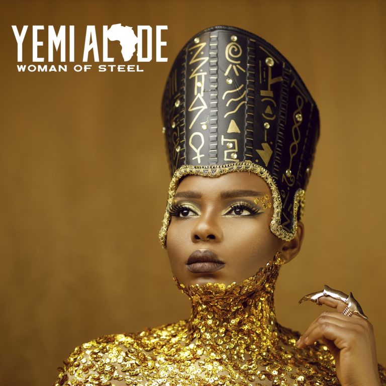 An image of Yemi Alade clad in an Egyptian headpiece and a black dress, complete with gold body glitter.